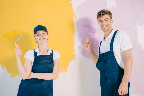 stock-photo-young-painters-overalls-holding-paint-rollers-smiling-camera